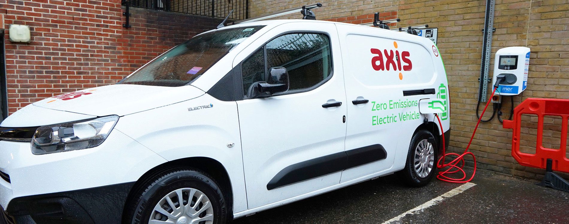 Axis white van in a parking space with an electric charger attached to the wall.