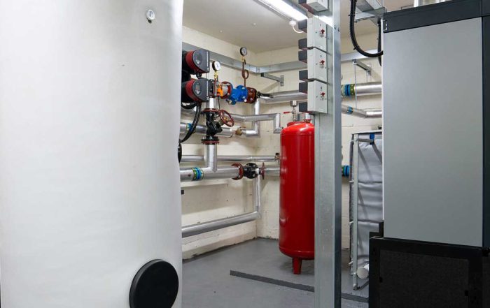 Boiler room of large white and red containers, grey pipework on the white walls and black flooring