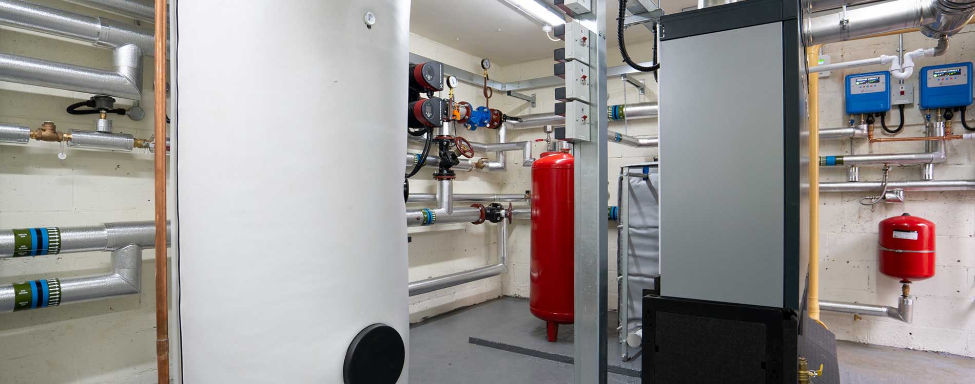 Boiler room of large white and red containers, grey pipework on the white walls and black flooring