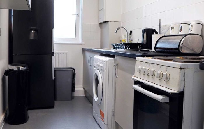 Kitchen with fridge, washing machine, oven, stove, sink. Black, white, grey colours