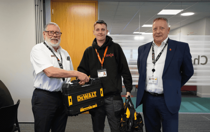 Two old man, and one young boy in the middle in an office. Suit, shirt, and black hoodie, holding a black tool kit