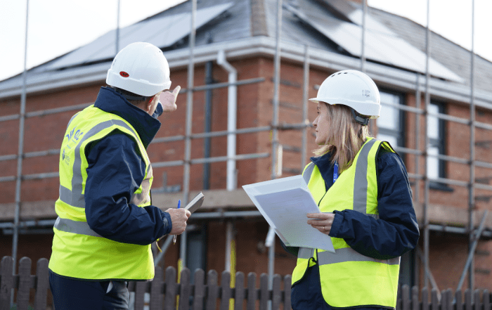 Two operative in yellow jackets and hard hats in front of scaffolded building
