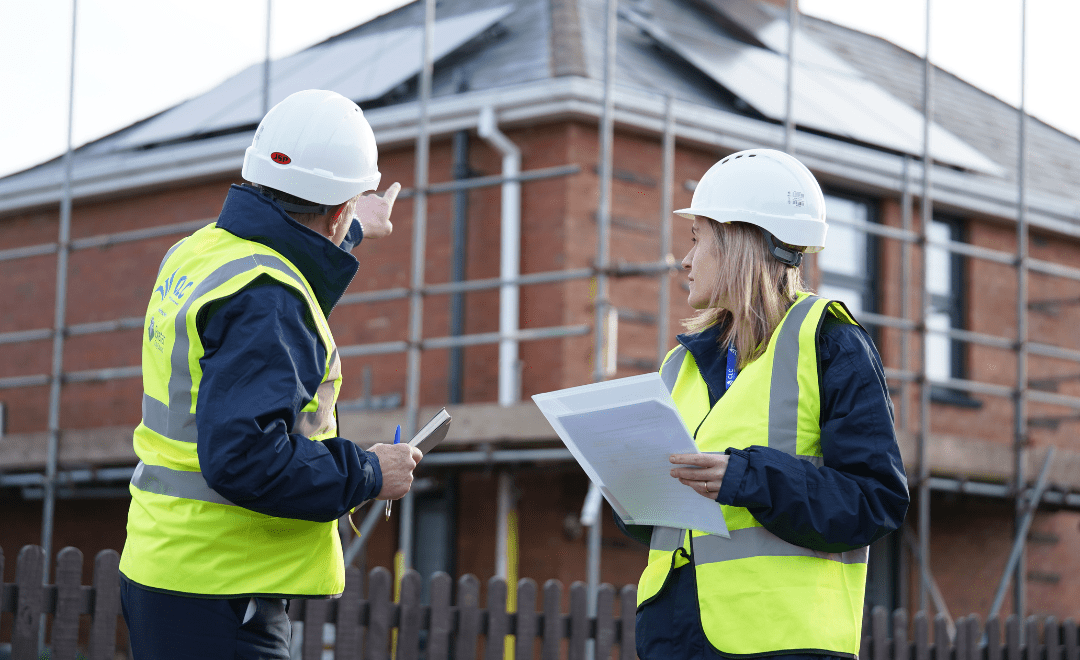 Two operative in yellow jackets and hard hats in front of scaffolded building