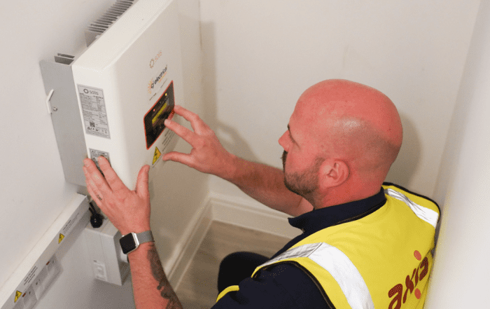 Workman with Axis vest, using his hands on an electrical system inside. Walls are white.