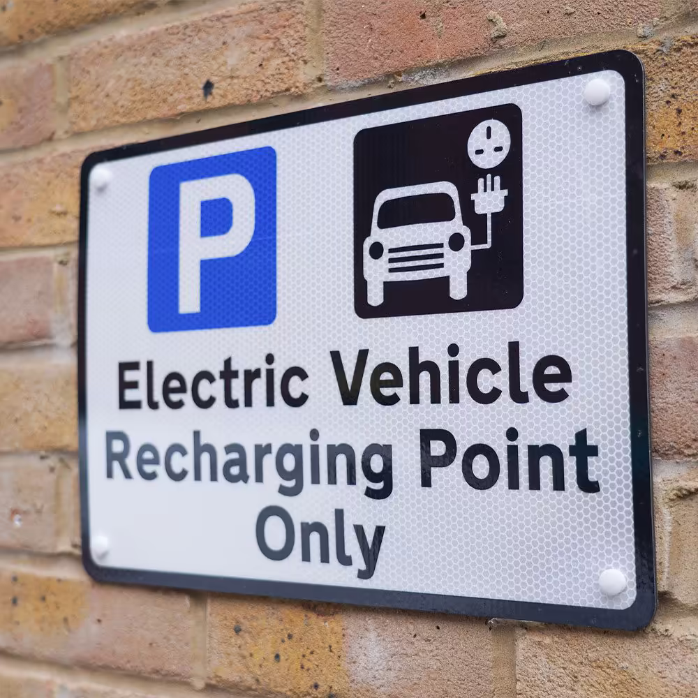 A close-up of a reflective sign on a brick wall that reads 'Electric Vehicle Recharging Point Only' with a graphic of a car and a charging plug.