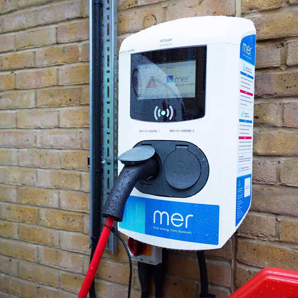 A wall-mounted 'Mer' electric vehicle charger with a red charging cable plugged in, showing the user interface and branding.