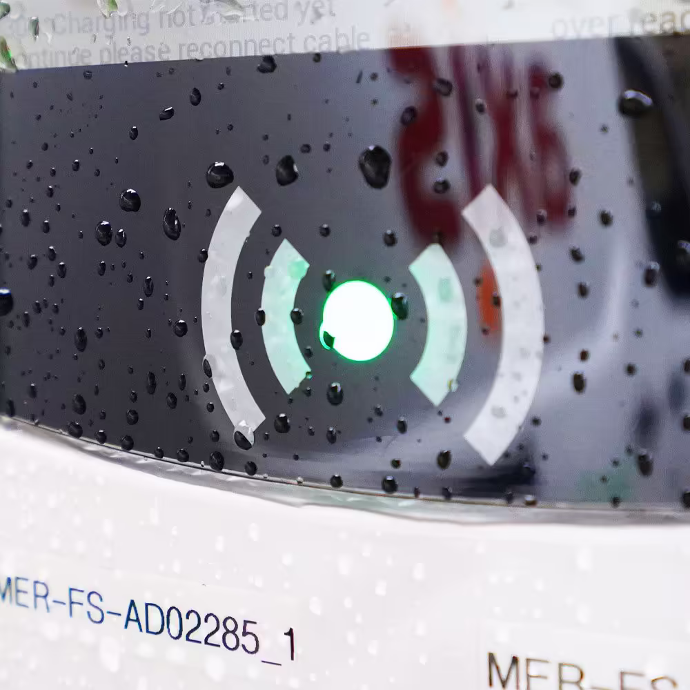 A macro shot of the status indicator on an EV charger, with a glowing green light in the center of a circular graphic, indicating charging is in progress.