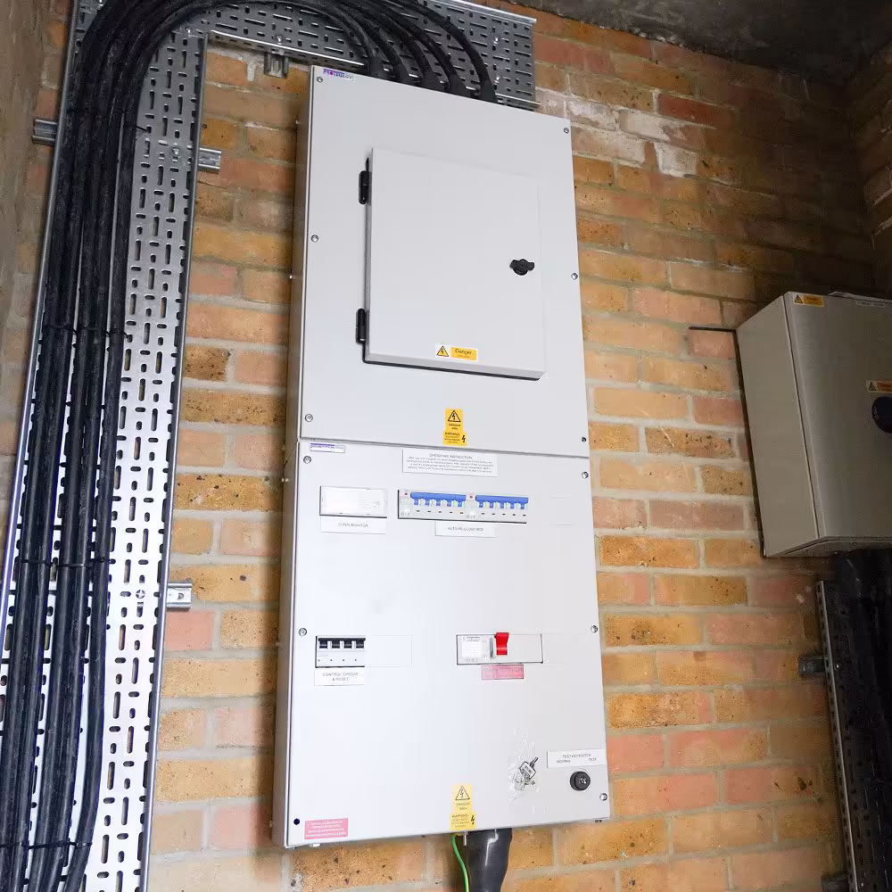 The main electrical distribution board for an EV charging system, professionally installed on a brick wall with neat cabling running in a metal tray.