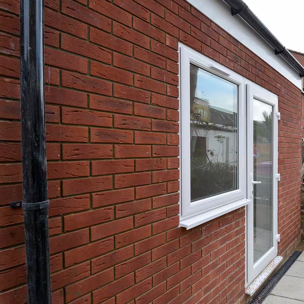 A close-up of a new red brick house extension, showing the quality of the brickwork and the installation of a new white window and glazed door.
