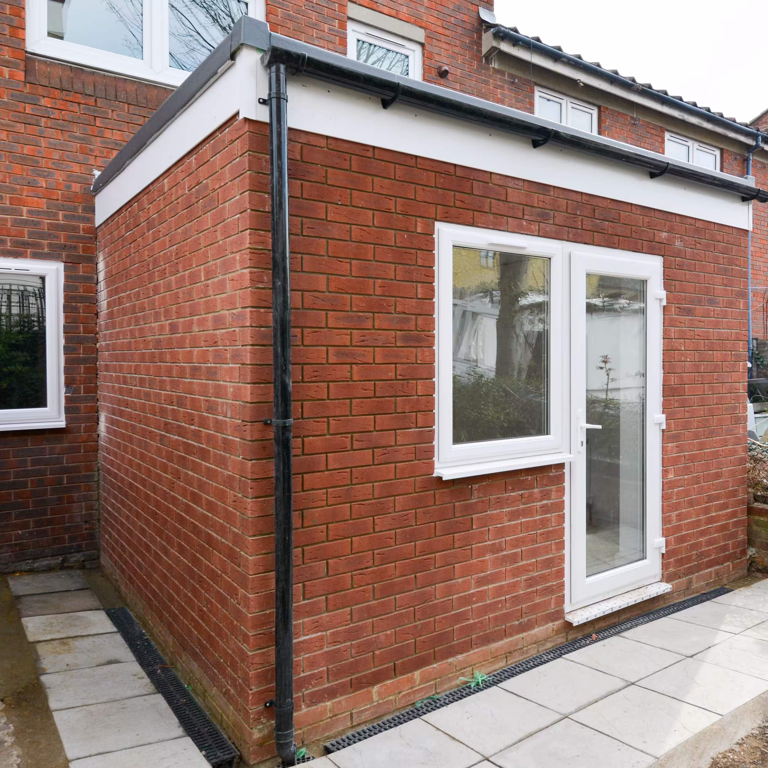 The completed exterior of a bespoke red brick, single-storey house extension, featuring a new patio and perimeter drainage.