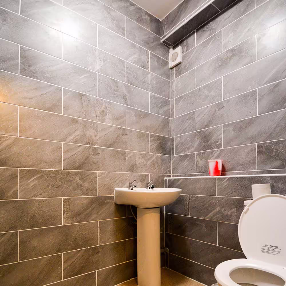 A new, fully tiled downstairs cloakroom created as part of the house extension, with modern grey stone-effect tiles, a toilet, and a pedestal sink.