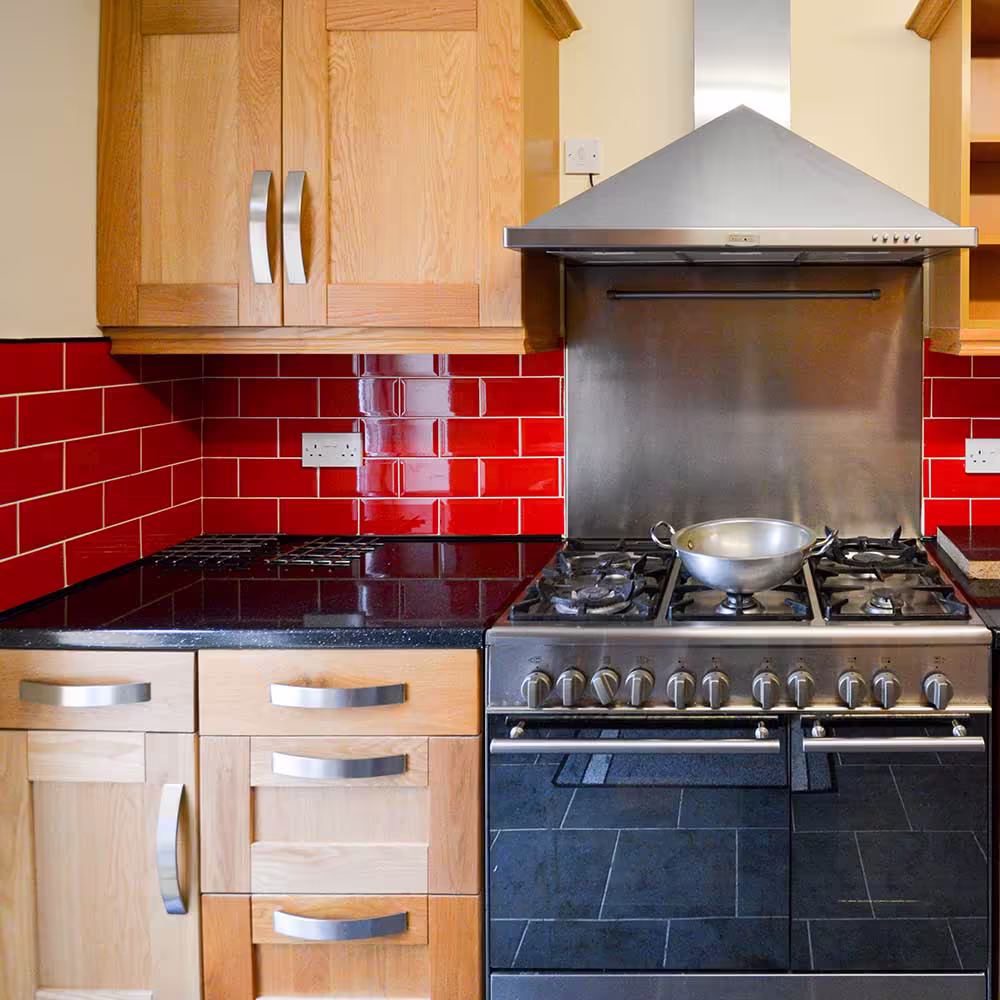A close-up of the high-end cooking area in the new kitchen extension, with a large stainless steel range cooker, gas hob, and a bold red tile splashback.