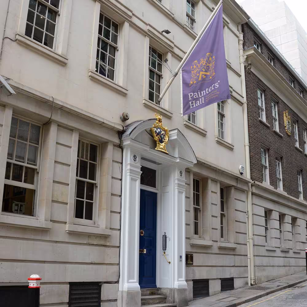 The restored exterior of the historic Painters' Hall in London, featuring a clean stone facade, a grand blue entrance door, and a purple flag flying.