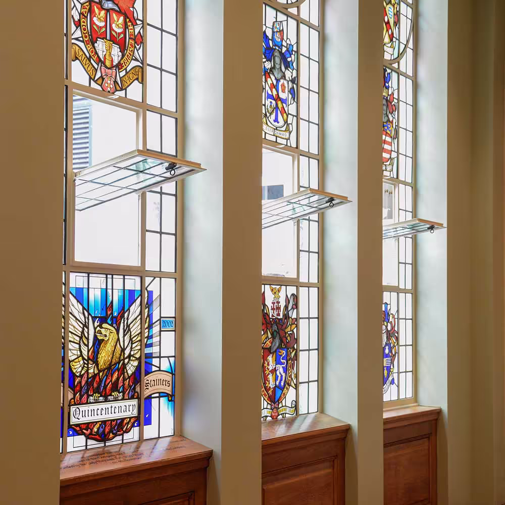 A detailed view of beautifully restored stained-glass windows in a historic hall, featuring colourful coats of arms and expertly repaired leaded panes.