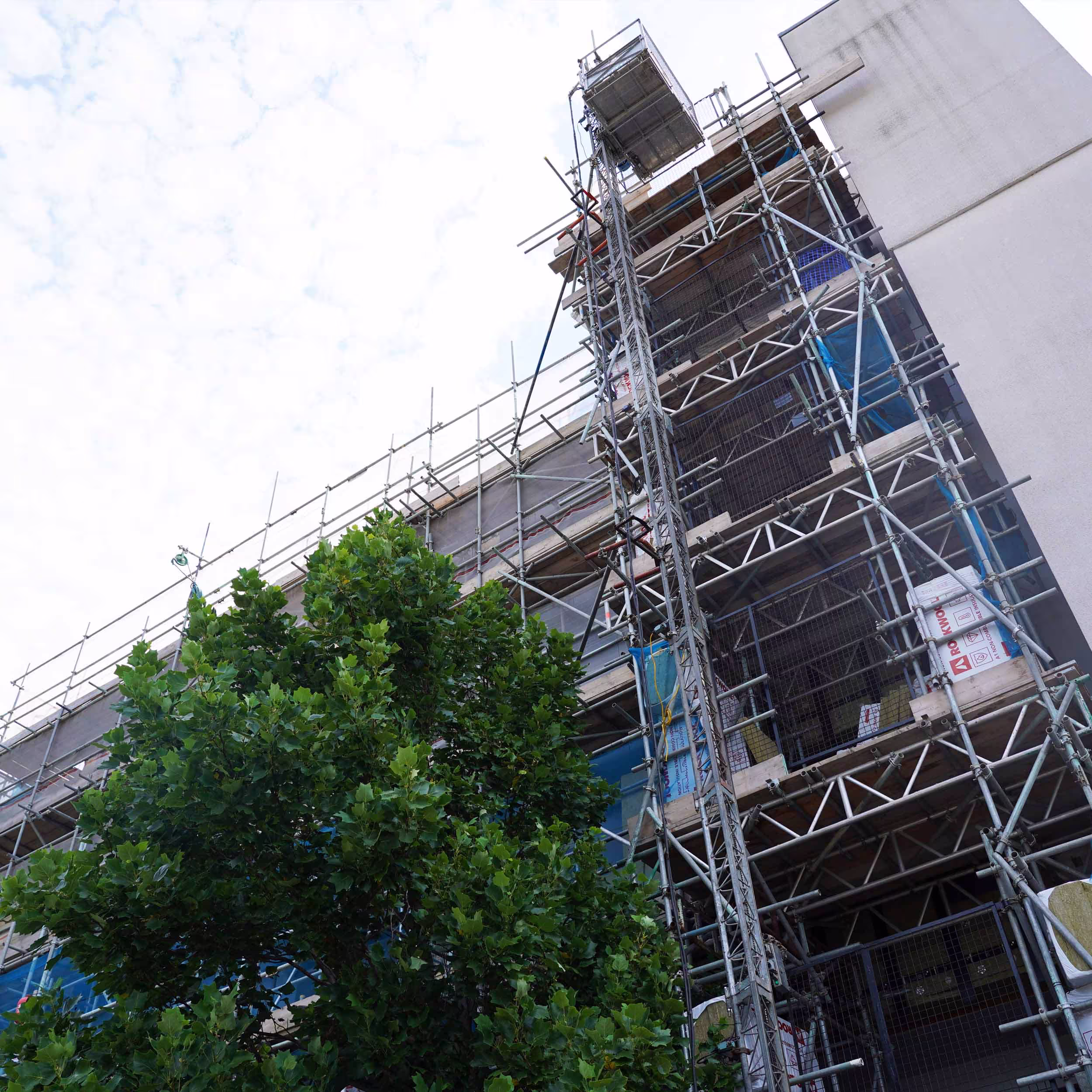 A low-angle view looking up at a high-rise residential block covered in scaffolding for essential cladding remediation works.