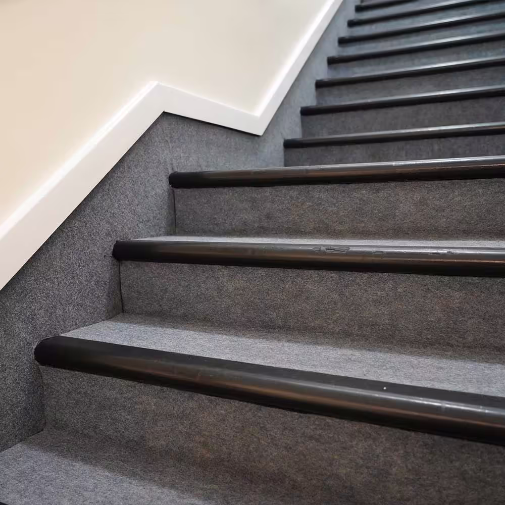 A newly refurbished communal staircase, fitted with durable grey carpet and high-visibility black safety nosings on each step for resident safety.