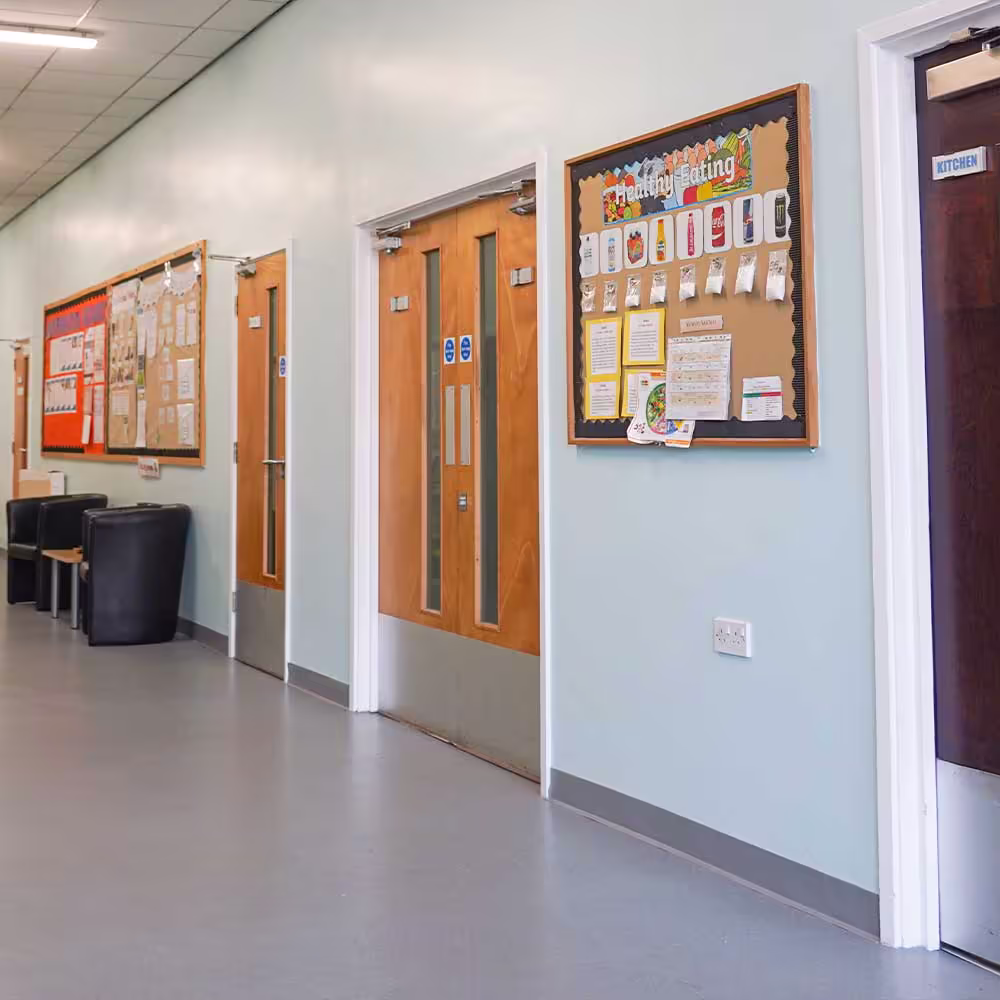 A newly decorated communal hallway in the community centre, showing the fresh light blue paint, multiple doors, and a 'Healthy Eating' noticeboard.