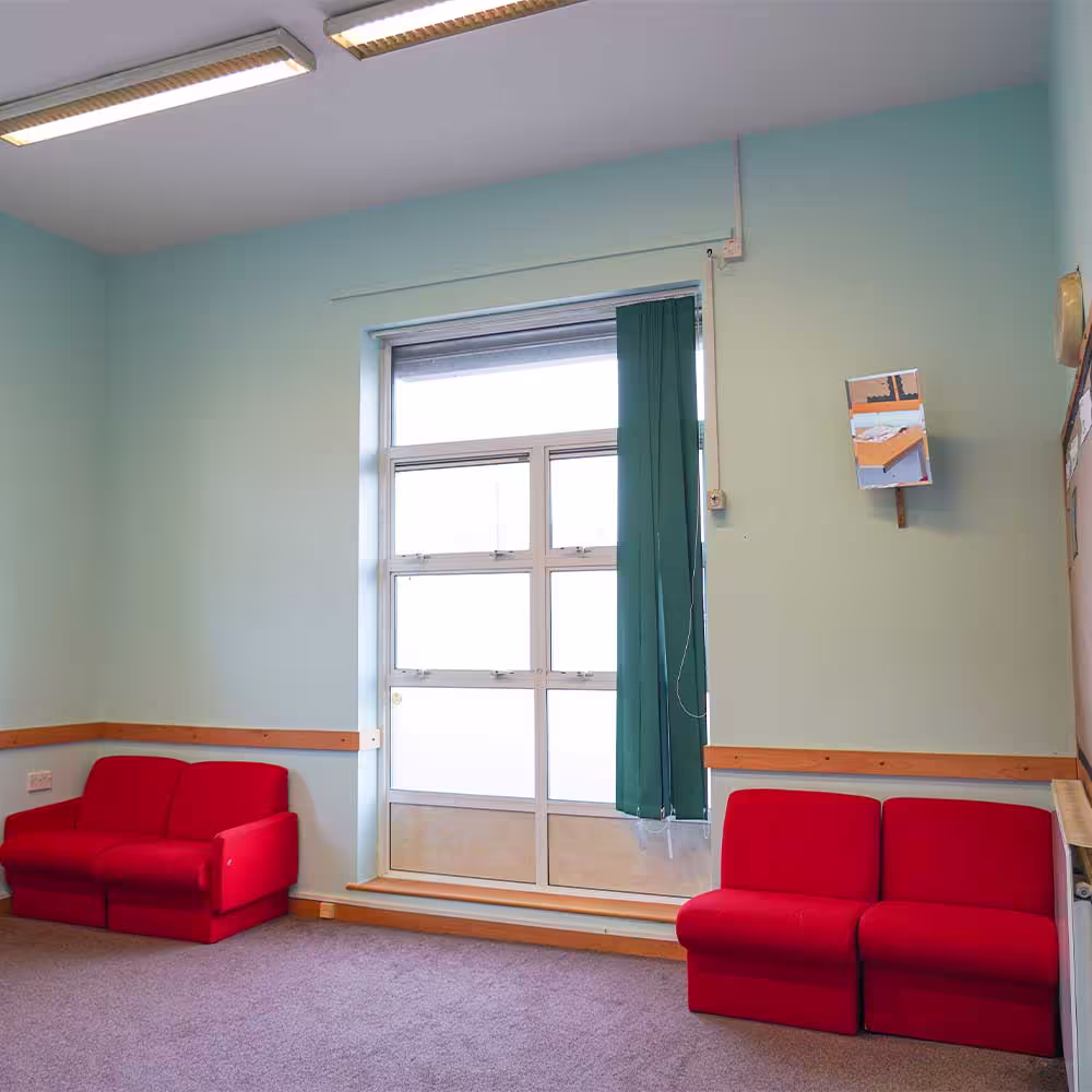 A redecorated multi-purpose room in the community centre, featuring freshly painted pale blue walls and comfortable red sofas for visitors.