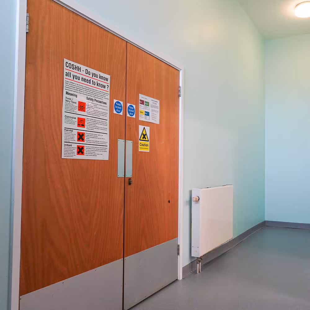 Newly decorated corridor walls surrounding a set of wooden storeroom doors, which display important COSHH and chemical safety notices for the community centre.