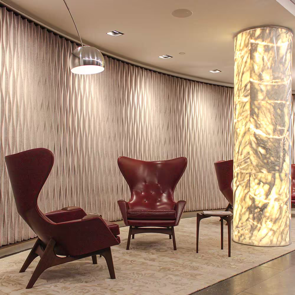 The luxurious waiting area of a refurbished corporate reception, with designer red leather armchairs, a stunning internally lit marble pillar, and a textured feature wall.