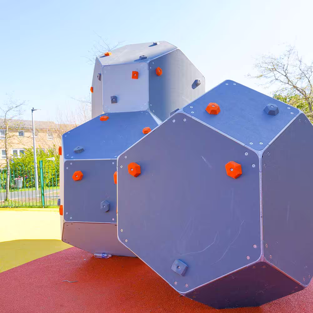 Modern geometric climbing boulders with orange handholds, installed in a children's play area on a soft rubber safety surface.