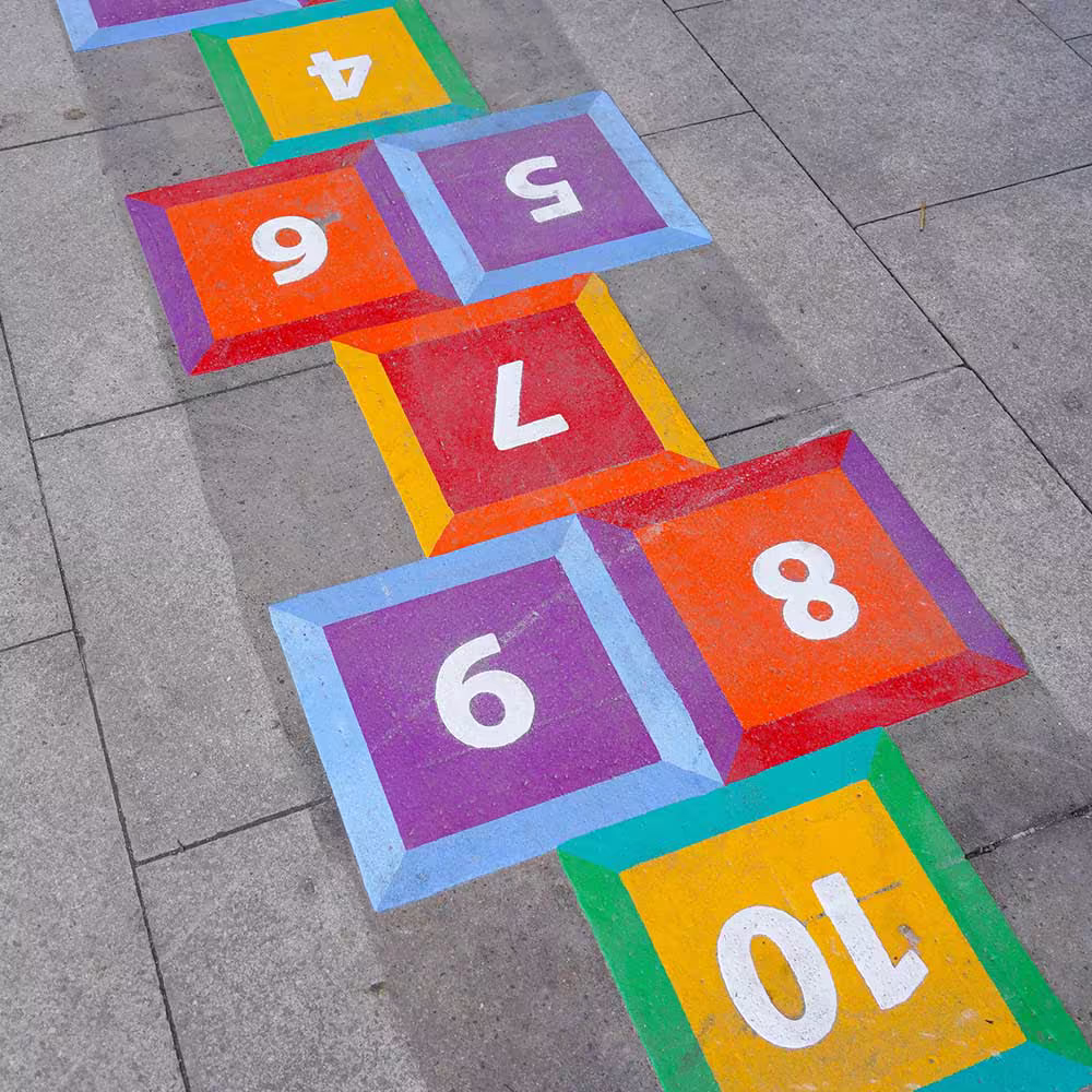 A vibrant and colourful hopscotch grid with a 3D effect, creatively painted onto a paved public space to encourage play.