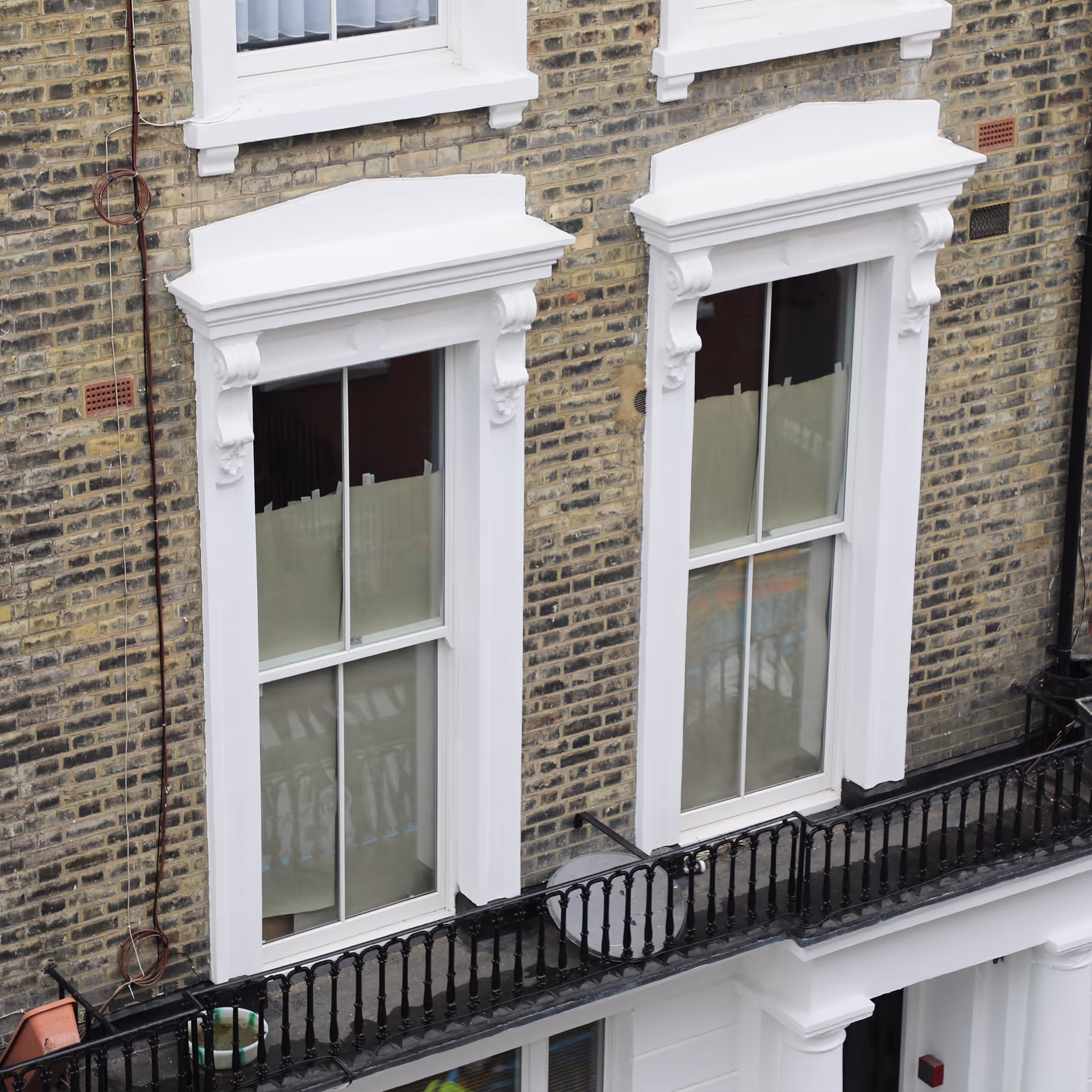 Two large, ornate sash windows on a period brick building, with their surrounds and sills expertly repaired and painted in brilliant white during external decorations.