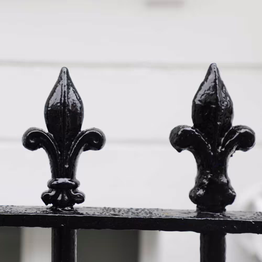 A close-up of two decorative fleur-de-lis finials on a cast iron railing, which have been restored and painted in high-gloss black as part of the cyclical decoration works.