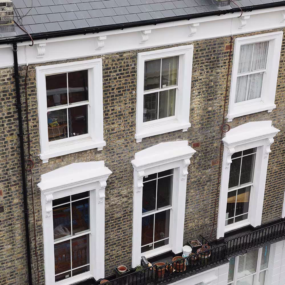 An aerial view of the facade of a period terraced house, showing the high-quality finish of the cyclical external decoration on the multiple freshly painted sash windows.