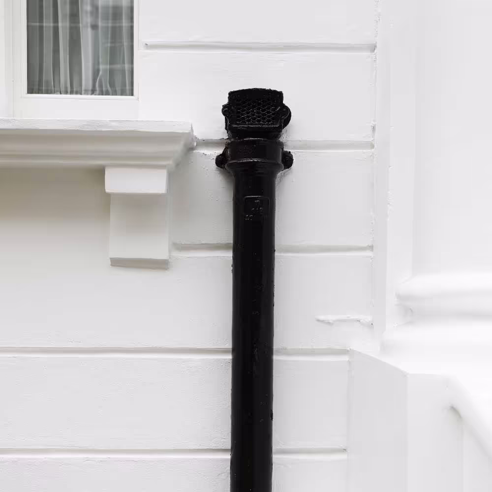 A minimalist detail shot of a freshly painted black downpipe against a clean white wall, highlighting the sharp, neat finish of the external decoration work.