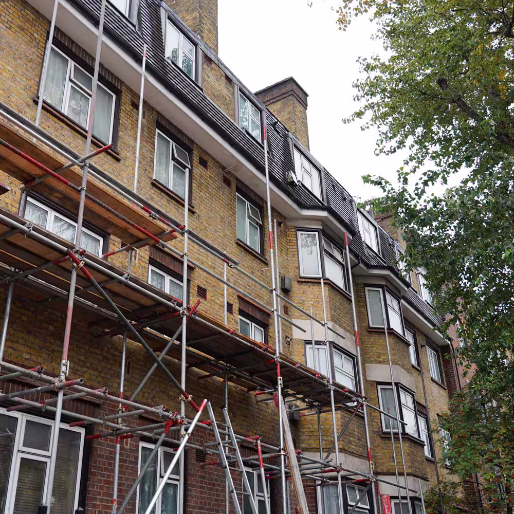 Low-angle view of a multi-story yellow brick apartment building covered in scaffolding during cyclical external improvements and renovations.