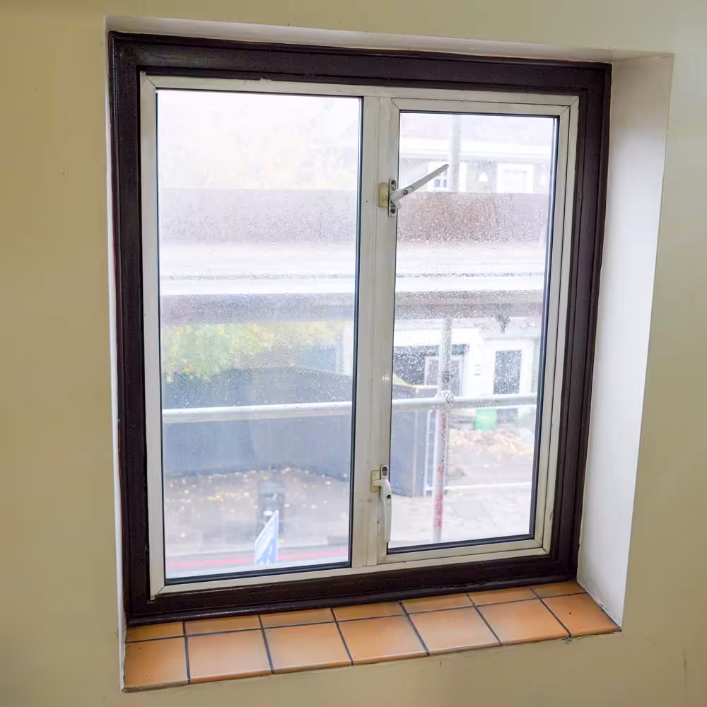 Interior view of an old window with a dark frame, looking out onto scaffolding, showing the 'before' state of a window replacement project.