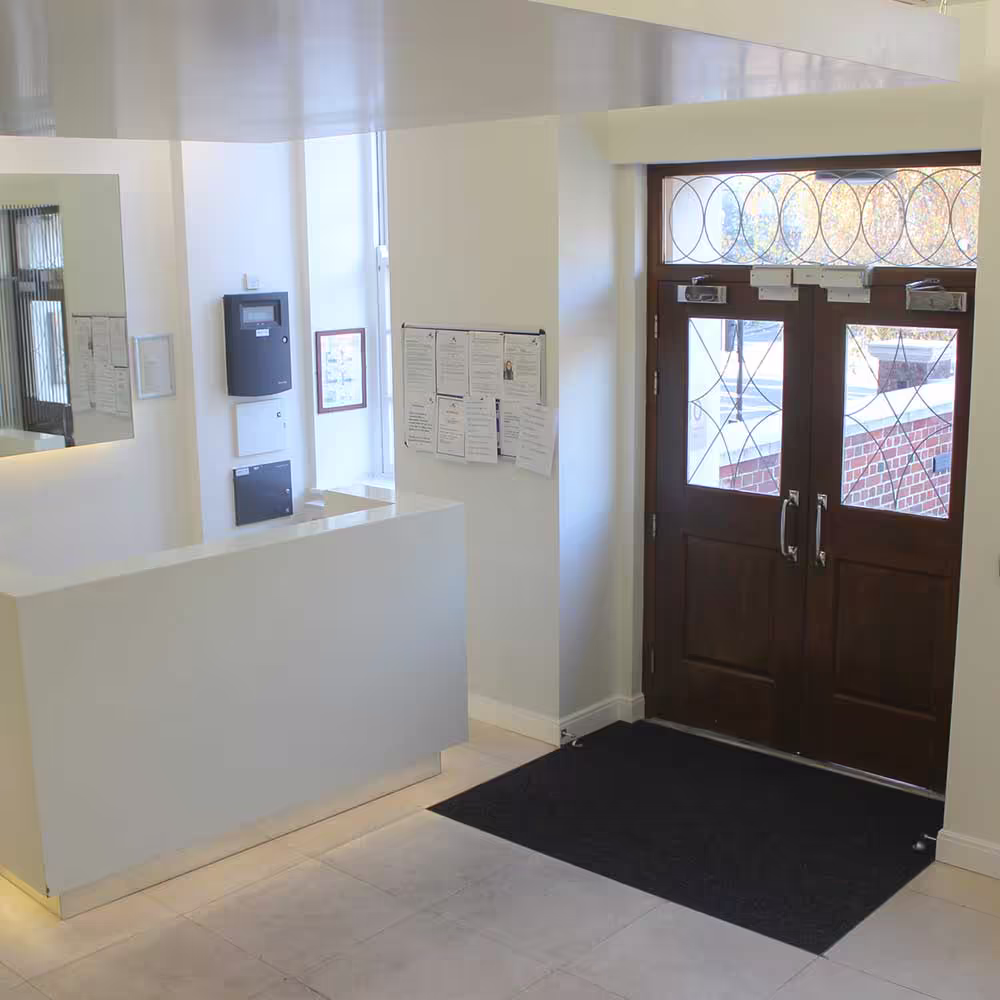 The bright and clean entrance lobby of a residential building after refurbishment, featuring a modern white reception desk, tiled flooring, and traditional wooden entrance doors.