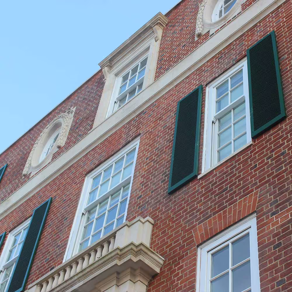 A close-up of the historic red-brick facade, showing the expertly maintained white sash windows and traditional dark green shutters following a cyclical maintenance programme.