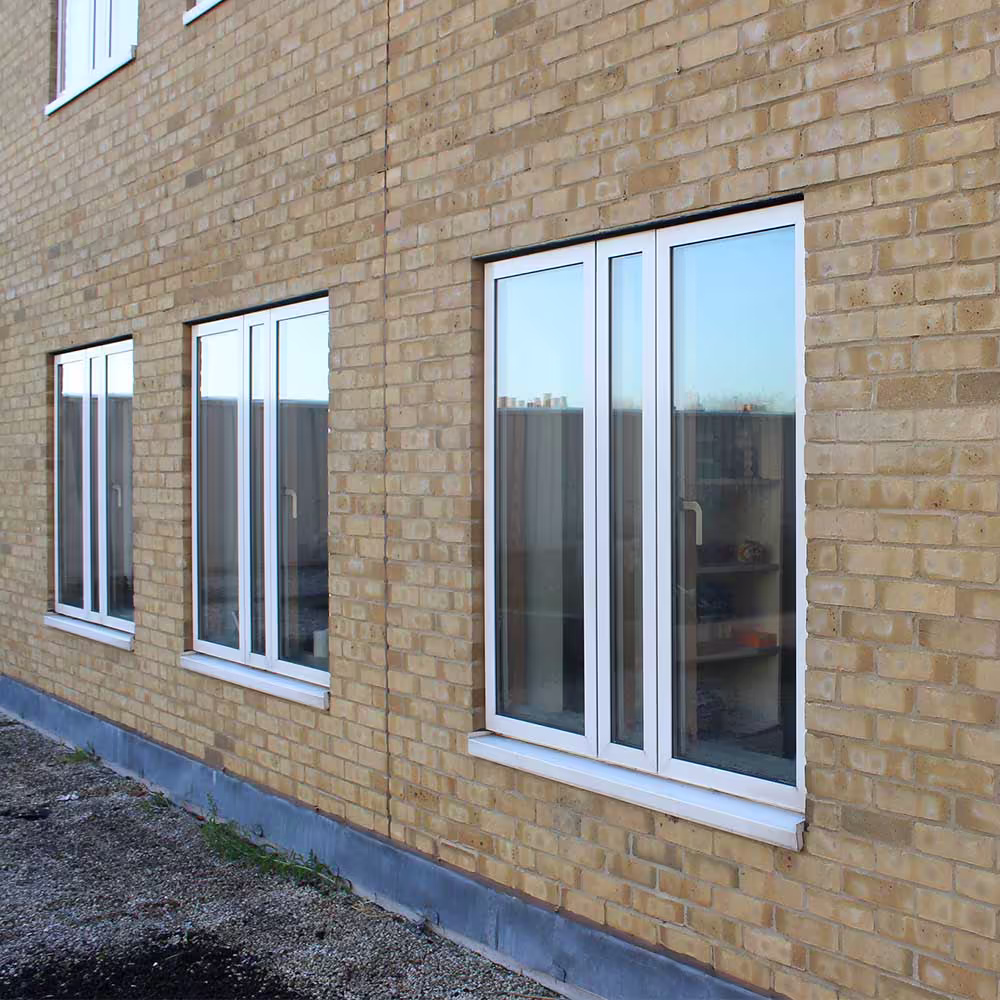 Newly installed modern white windows on a clean, yellow brick wall, showing the window replacement works completed during a cyclical maintenance programme.