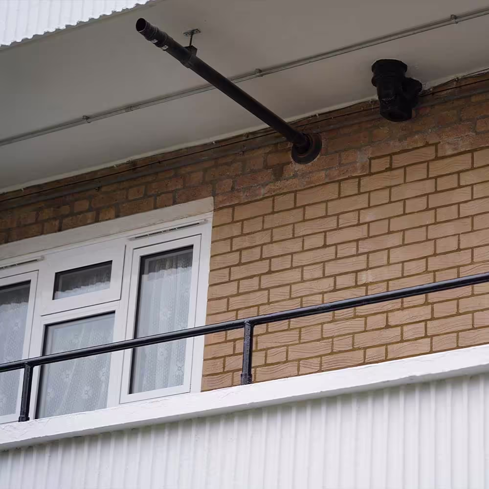 Newly re-decorated external features on a residential block, including a freshly painted black metal railing and drainage pipe against a clean white soffit.