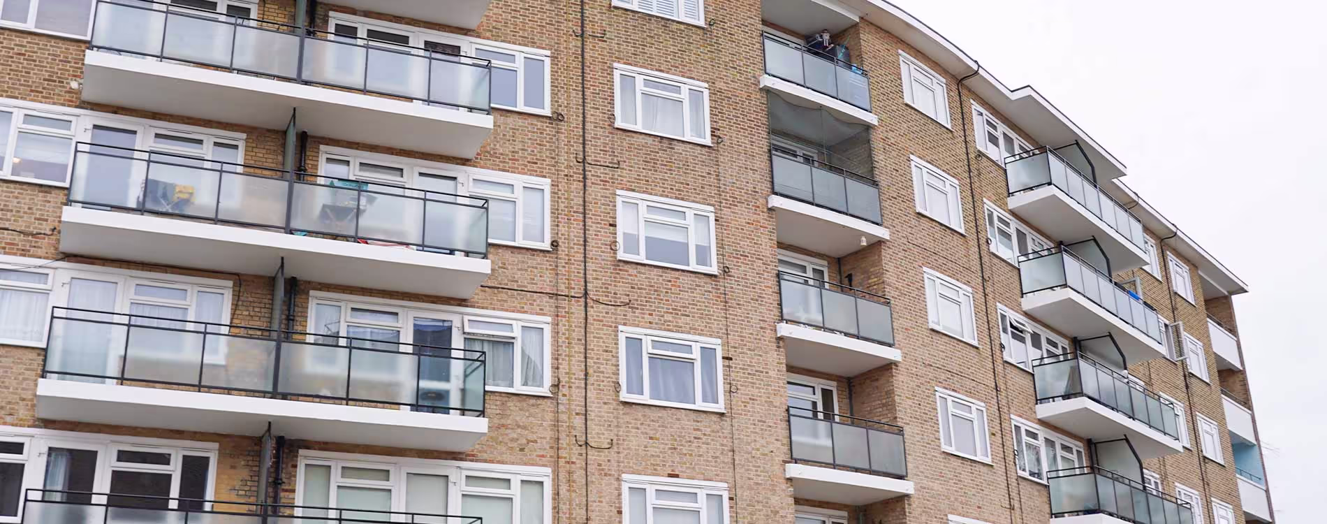 The well-maintained exterior of a multi-storey brick apartment block, showing the clean facade and modern glass balconies after a cyclical repairs and re-decoration project.