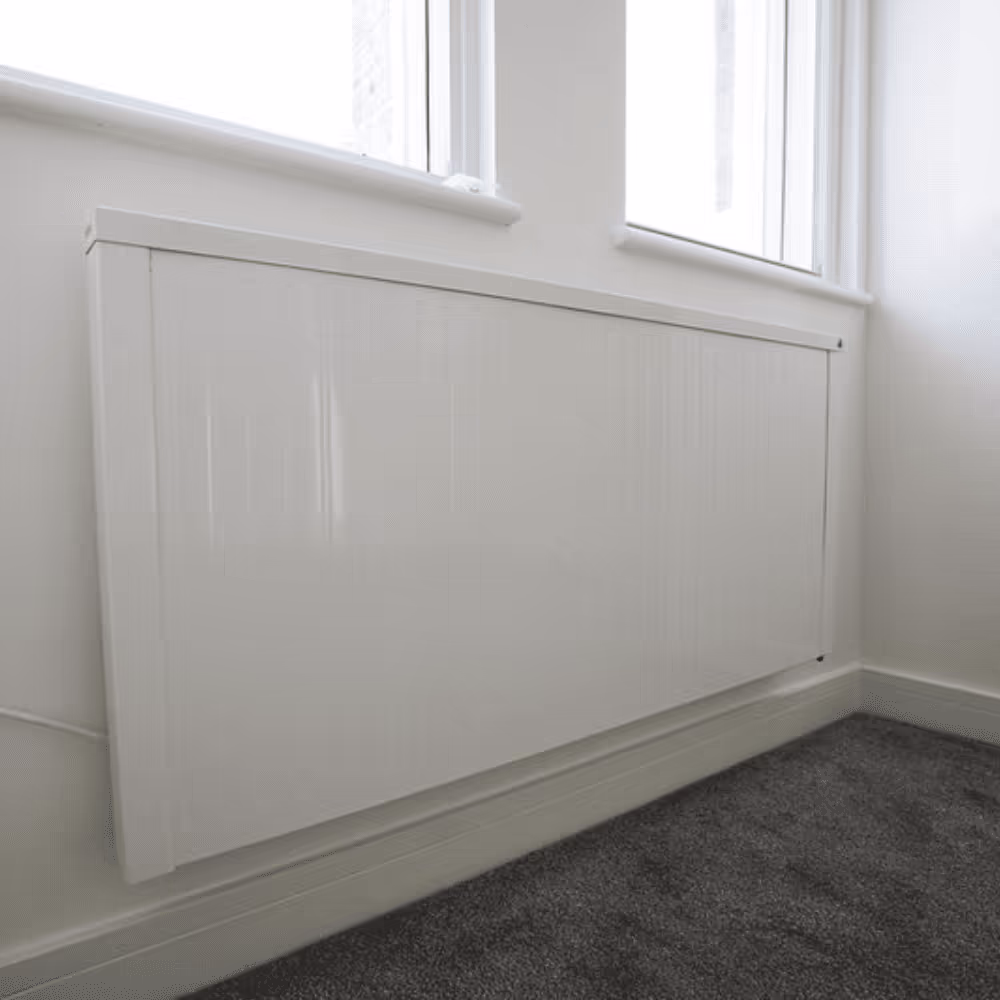 A sleek, white, low-surface-temperature radiator installed in a refurbished room with dark grey carpet, showcasing an energy-efficient heating upgrade.