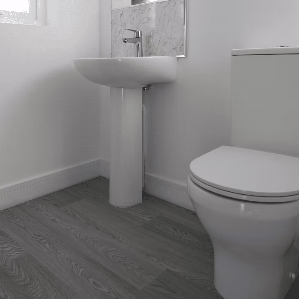 A modern, newly installed bathroom with a white toilet and pedestal sink, grey wood-effect flooring, and a marble-effect splashback, reflecting a full property refurbishment.