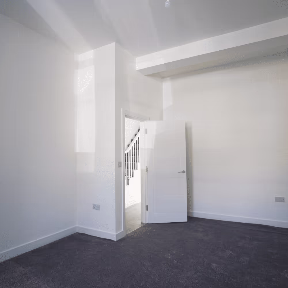 A bright and spacious, newly decorated room with fresh white walls and grey carpet, showing the results of a property deconversion project.