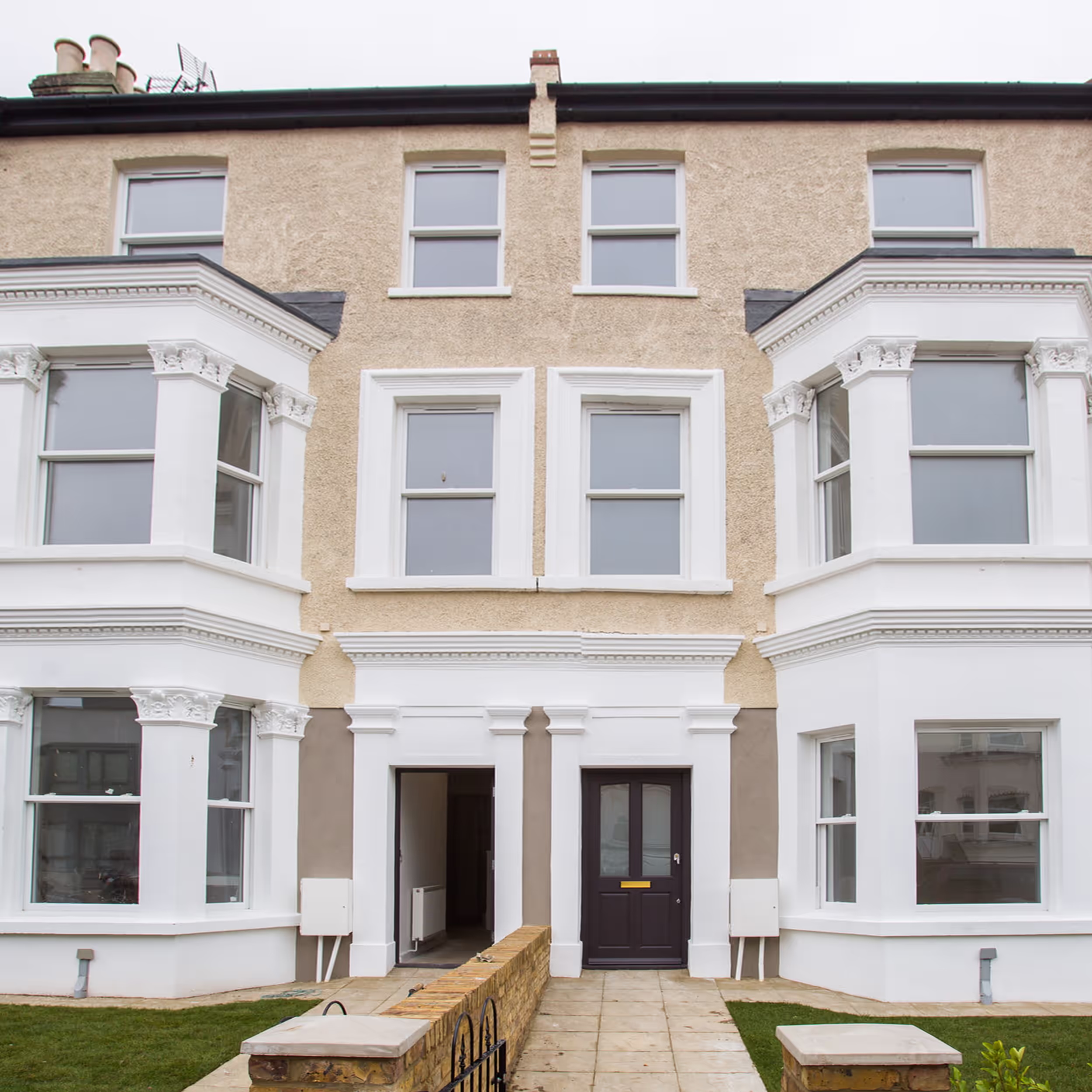 The fully restored front facade of a Victorian property that has been converted into modern apartments, featuring new windows, doors, and pristine paintwork.