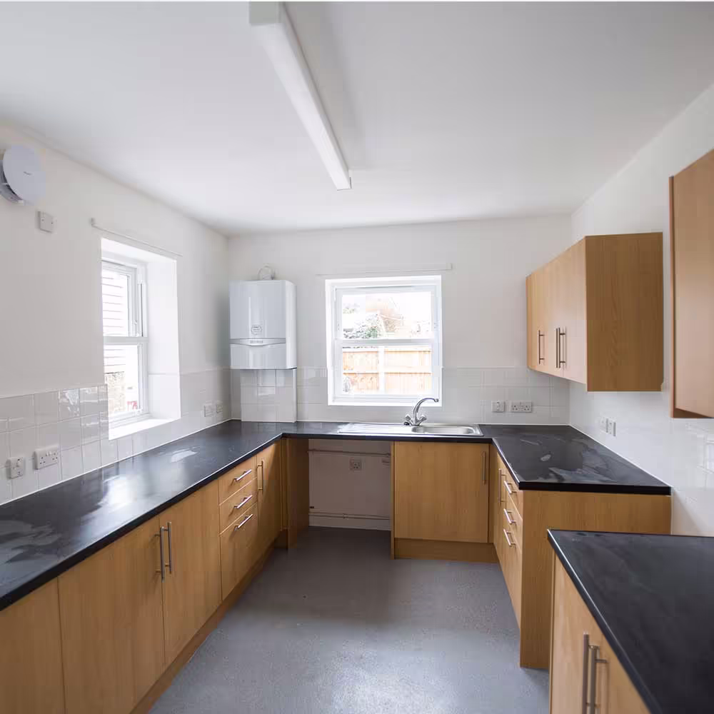 A spacious, newly fitted kitchen within a converted property, featuring modern U-shaped oak-effect cabinets, dark worktops, and a new energy-efficient boiler.