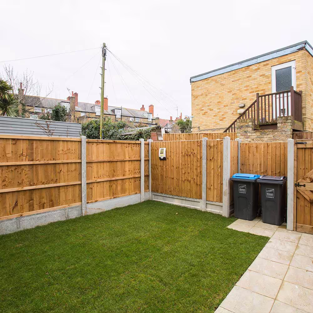 The newly landscaped back garden of a converted flat, with fresh turf, a paved patio area, and a new wooden privacy fence, creating a usable outdoor space.