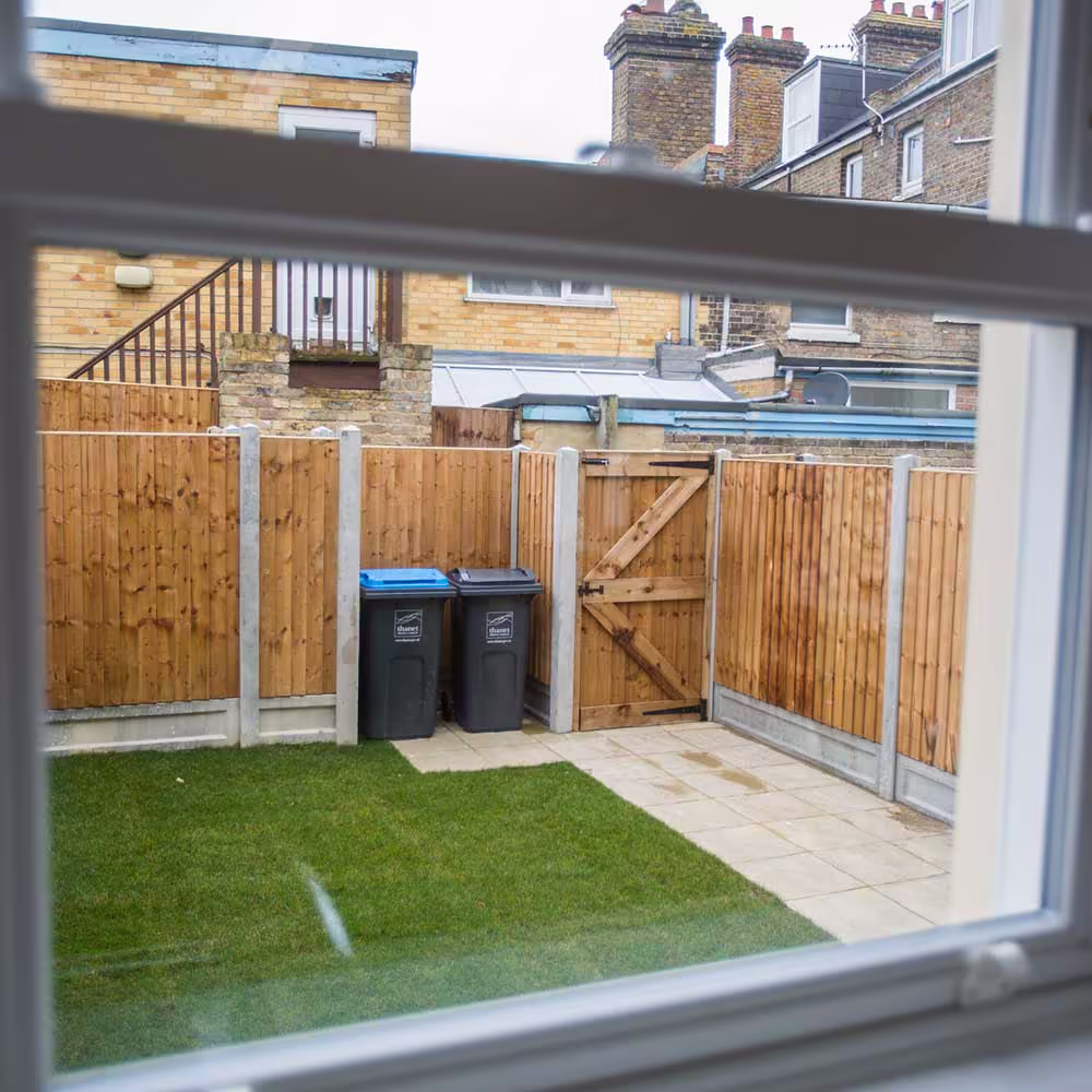 The view from a window of a newly converted flat, looking out onto a neat private garden with a new lawn, fence, and patio.