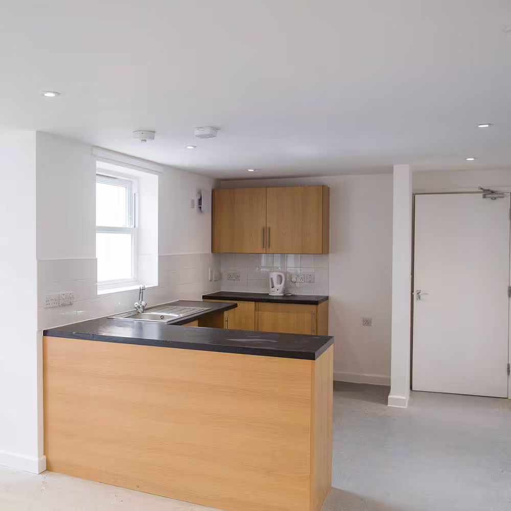 A modern, open-plan kitchen in a converted flat, featuring a breakfast bar for casual dining, oak-effect cabinets, and recessed ceiling spotlights.