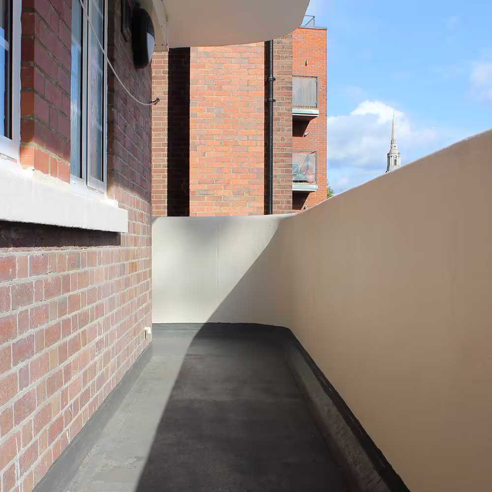 A clean, redecorated apartment balcony with new asphalt flooring and freshly painted cream-coloured walls, overlooking neighbouring buildings.