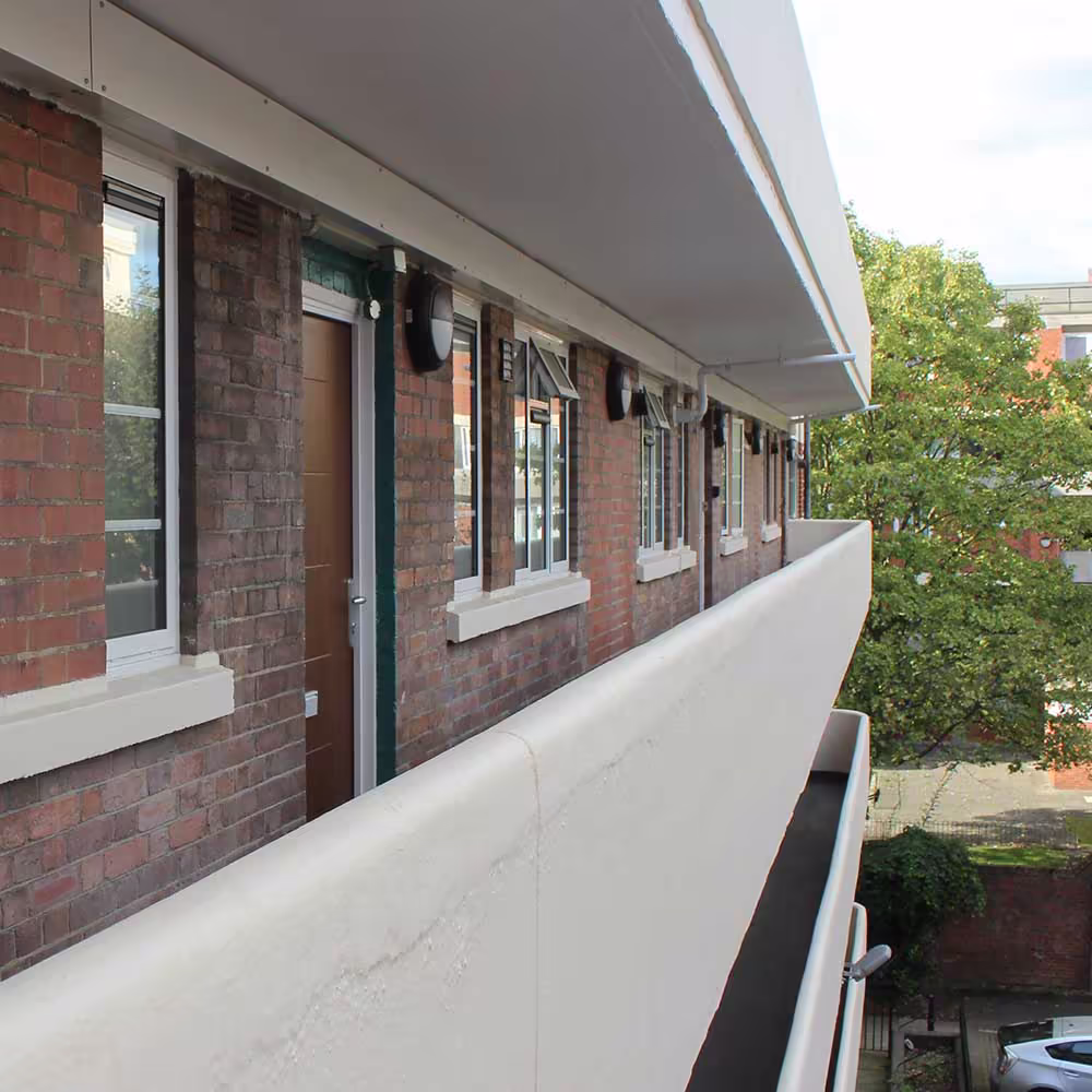 View along a redecorated external walkway of a brick apartment building, featuring a clean, curved, off-white balcony wall.