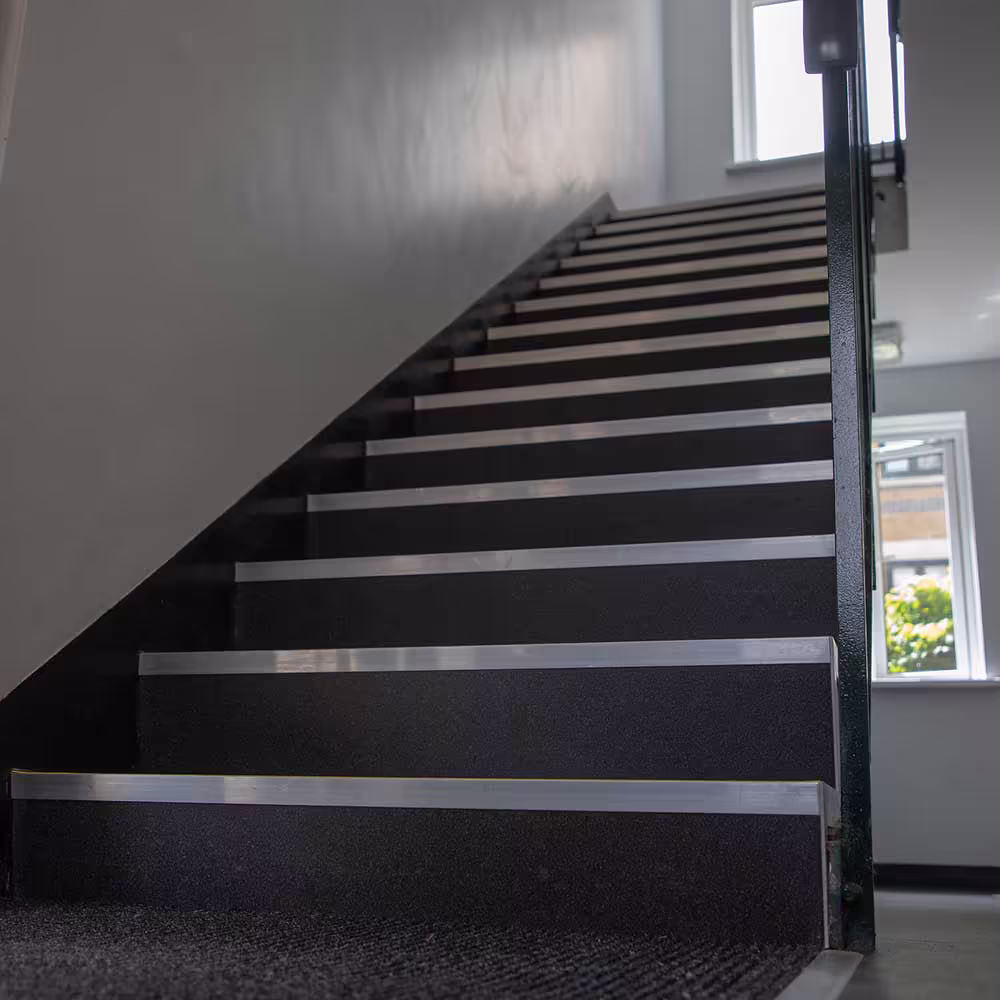 A clean and safe communal staircase after refurbishment, featuring hard-wearing carpet and prominent metal stair nosings as part of a maintenance project.
