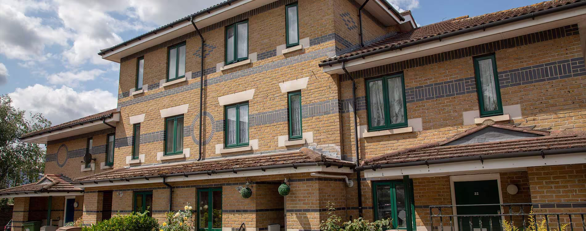 The well-maintained exterior of a modern residential building, showing the clean brickwork and green windows after an external maintenance programme.