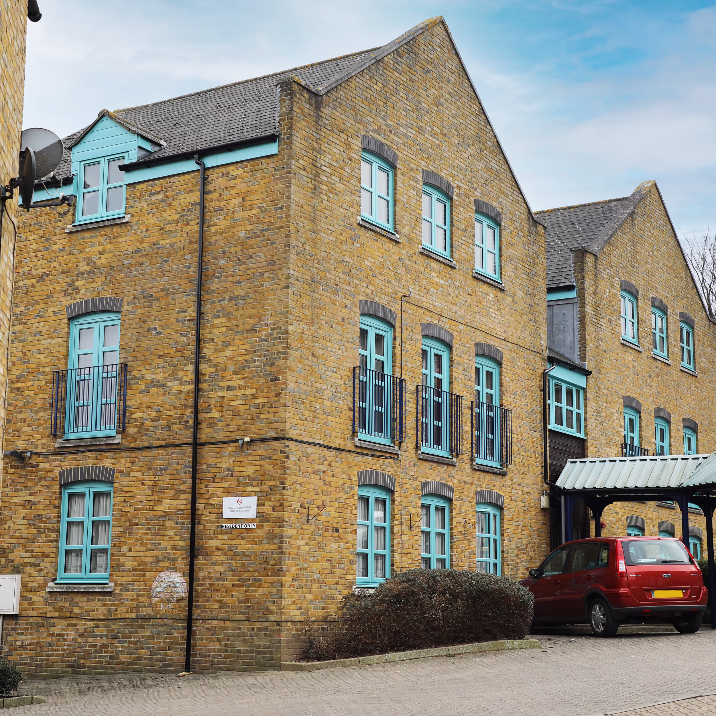 A modern yellow brick residential block after receiving external property services, highlighting the uniform finish of the distinctive turquoise windows across the building.